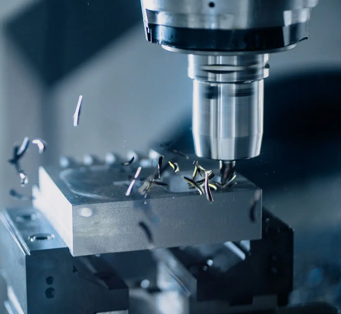Freeskop van een CNC-machine bewerkt een metalen blok; de spanen vliegen in het rond