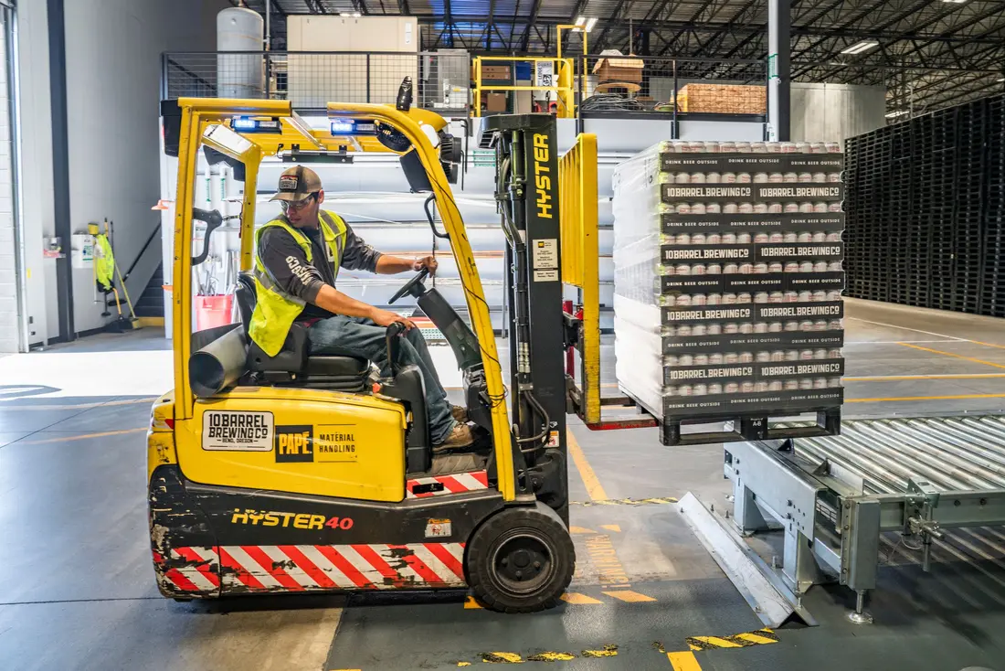 Heftruck zet een pallet met dozen op een rollenbaan in een magazijn